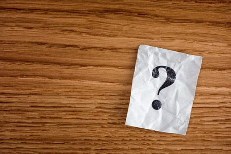 Paper note with question mark on wooden board. Close up
