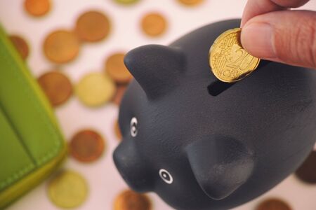 Person putting 20 euro cent coin into black piggy bank. Close up.