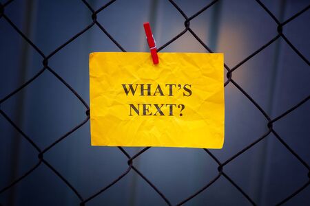 Paper note with question What is next hanging on a metal mesh fence. Close up.の写真素材
