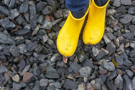 Person standing on stones in yellow boots. Close up.
