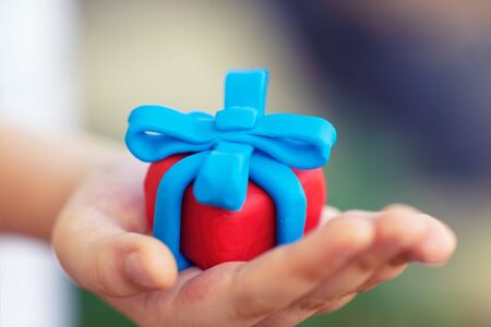 Young boy holds gift wrapped with blue ribbon. Shallow depth of field. Close up. Gift box and ribbon are made out of play clay (plasticine).の写真素材