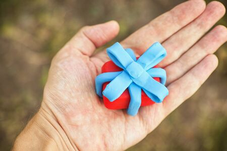 Person holding gift wrapped with blue ribbon. Shallow depth of field. Close up. Gift box and ribbon are made out of play clay (plasticine).の写真素材