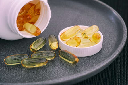 Fish oil capsules spilling out of bottle (Omega 3 supplement). Close up.