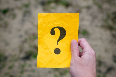Man holding yellow paper note with Question mark in his hand. Close up.の写真素材