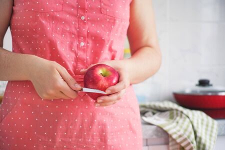 Woman standing in kitchen and holding an apple and a knife in her hands. Healthy breakfast.の写真素材