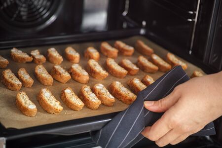 Person taking out baked cantuccini cookies from oven. Italian almond cookies.の写真素材