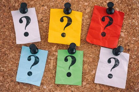 Colorful crumpled paper notes with question marks on a cork board. Closeup.