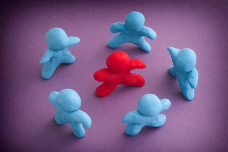 Blue plasticine people surrounding red plasticine person. Stand out from the crowd. Bullying concept. Close up.の写真素材