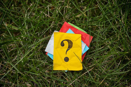 Pile of colorful paper notes with question marks on green grass. Close up.の写真素材