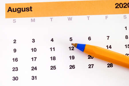A ballpoint pen lying on a calendar that is showing august month. Close up.