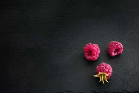 Organic raspberries on a black stone background. Low Key. Close up.