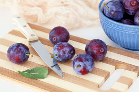 Plums lying on a cutting board with a kitchen knife. Close up.の写真素材