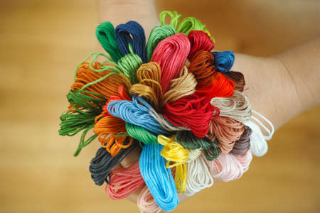 Person holding many colored cross stitch threads in her hands. Close up.