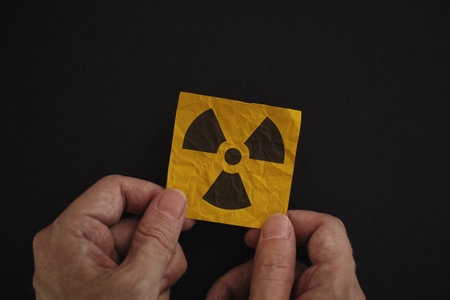 Man holding a radiation warning sign in his hands against a black background. Low key.