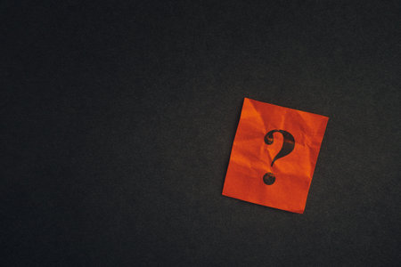 Red paper note with question mark on a black background. Low key. Close up.