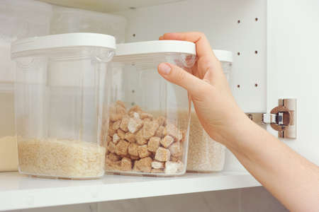 Woman taking brown cane sugar from a kitchen cupboard. Close up.の写真素材