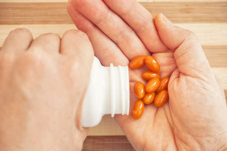 Woman taking Coenzyme Q10 pills out of a bottle. Close up.の写真素材