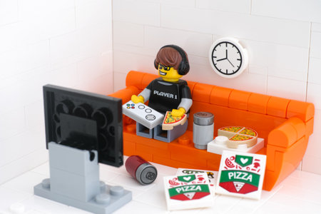 Tambov, Russian Federation - February 24, 2021 Lego video game guy minifigure sitting on a couch playing video games and eating pizza.のeditorial素材