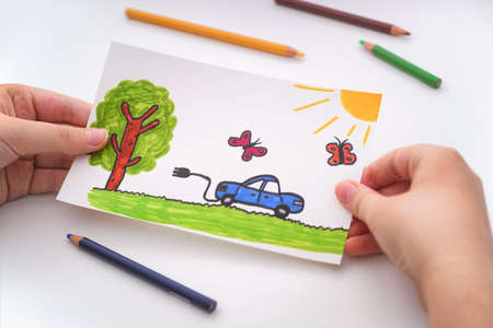 Young boy holding a childlike drawing of an electric car going for a drive outdoors in his hands. Close up.の写真素材