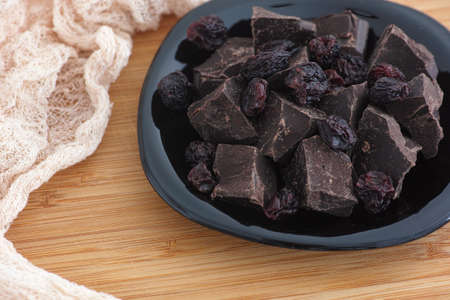 Pieces of homemade broken dark chocolate and raisins in a black plate. Close up.