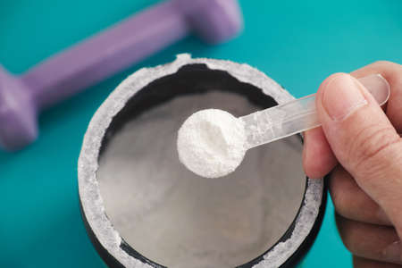 AAKG supplement. Man holding a scoop of AAKG powder in his hand. Close up.