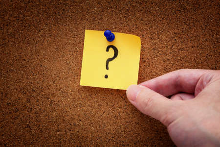 A man taking a pinned paper note with a question mark from a cork board. Close up.の写真素材