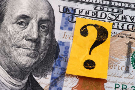 A one hundred dollar bill and a yellow paper note with a question mark on it. Closeup.
