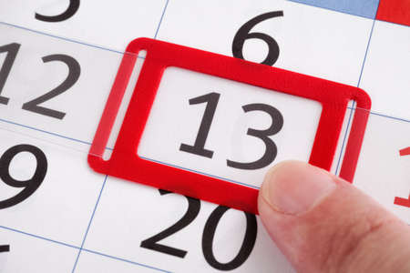 A finger pointing at the 13th day of the month on a calendar. Close up.