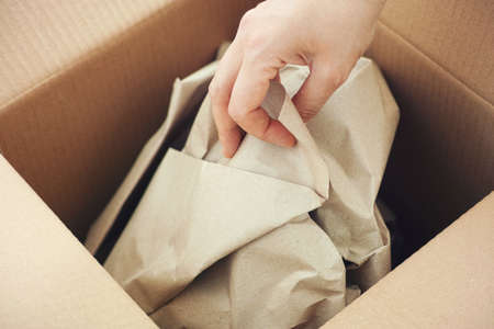 A woman taking crumpled paper out of an open cardboard box. Close up.の写真素材