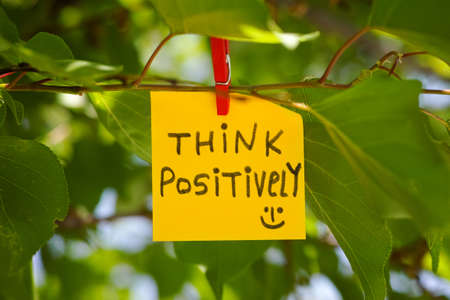 A paper note with "think positively" written on it attached to a tree with a clothes pin. Close up.の写真素材