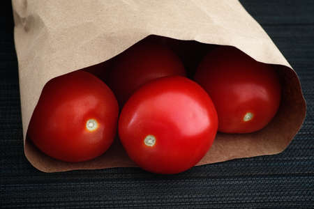Freshly harvested red tomatoes in a paper bag. Low key. Close-up.の写真素材