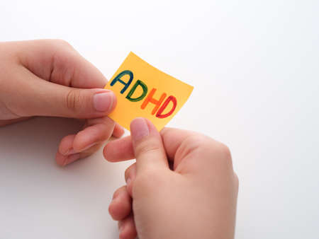 ADHD. A child holding a yellow paper note in his hands with the abbreviation ADHD on it. Close up. ADHD is Attention deficit hyperactivity disorder.の写真素材