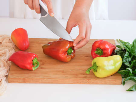 A woman cutting bell peppers with a knife in a kitchen. Close up.の写真素材