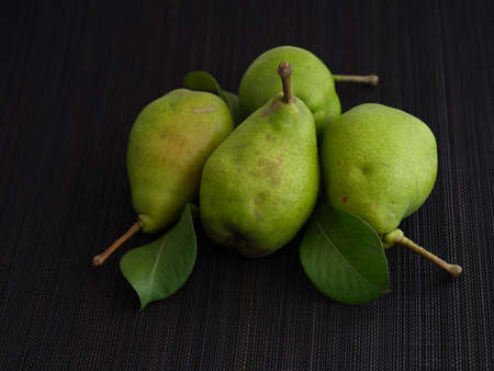 Four fresh organic pears with leaves on a black mat. Low key. Close up.の写真素材