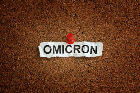 The word Omicron on a piece of paper that is pinned to a cork board. Omicron variant of COVID-19. Close up.の写真素材