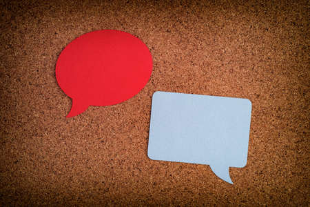 Two speech bubbles, one round, one square laying on a cork board. Close up.の写真素材