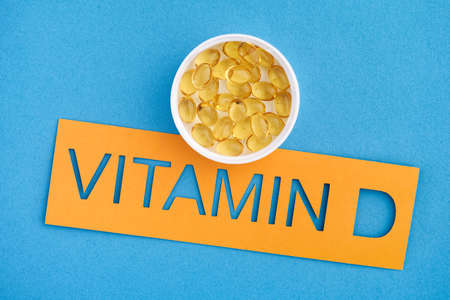 The word Vitamin D with a small cup of Vitamin D3 capsules on it. close up.の写真素材