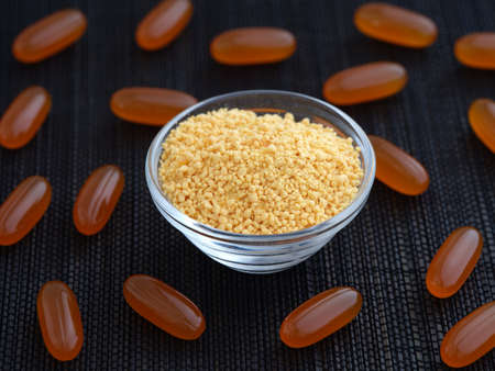 Soy lecithin in a glass bowl with soy lecithin softgels around it. low key. close up.