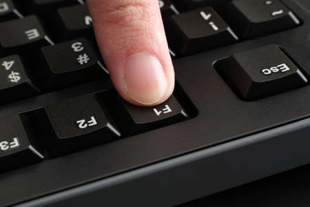 A finger pushing the F1 key on a black computer keyboard. close up.