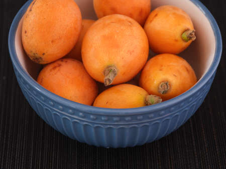 Loquat fruits in a blue bowl. low key. close up.