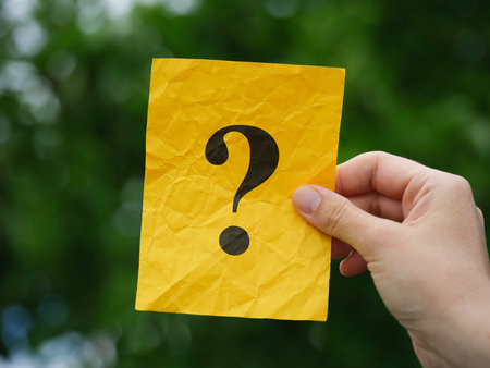 A woman holding a yellow note paper with a question mark on it in her hand over a background of...