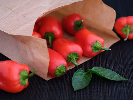 Some red bell peppers lying in a paper bag with some leaves near it. Shallow depth of field. close up.の写真素材