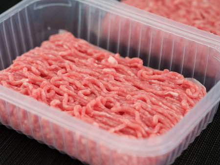 Two plastic containers with minced pork and beef in them lying on a black mat. Close up.の写真素材