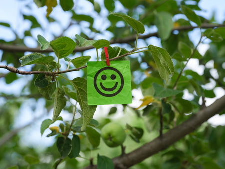 A green paper note with a happy face on it attached to a tree branch with a clothes pin. Close up.の写真素材