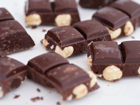 Broken pieces of  dark chocolate with hazelnuts on a white plate. Close up.