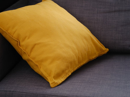 A yellow cushion on a gray couch. Close up.の写真素材