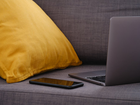 A laptop with a smartphone on a gray couch. Close up.の写真素材