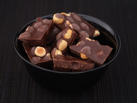 Pieces of broken dark chocolate with hazelnut in a black bowl. Close up.の写真素材
