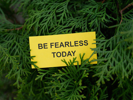 A yellow paper note with the phrase Be Fearless Today on it hanging on a arborvitae tree. Close up.の写真素材