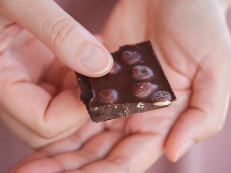 A woman holding a piece of dark chocolate with hazelnut in her hand. Close up.